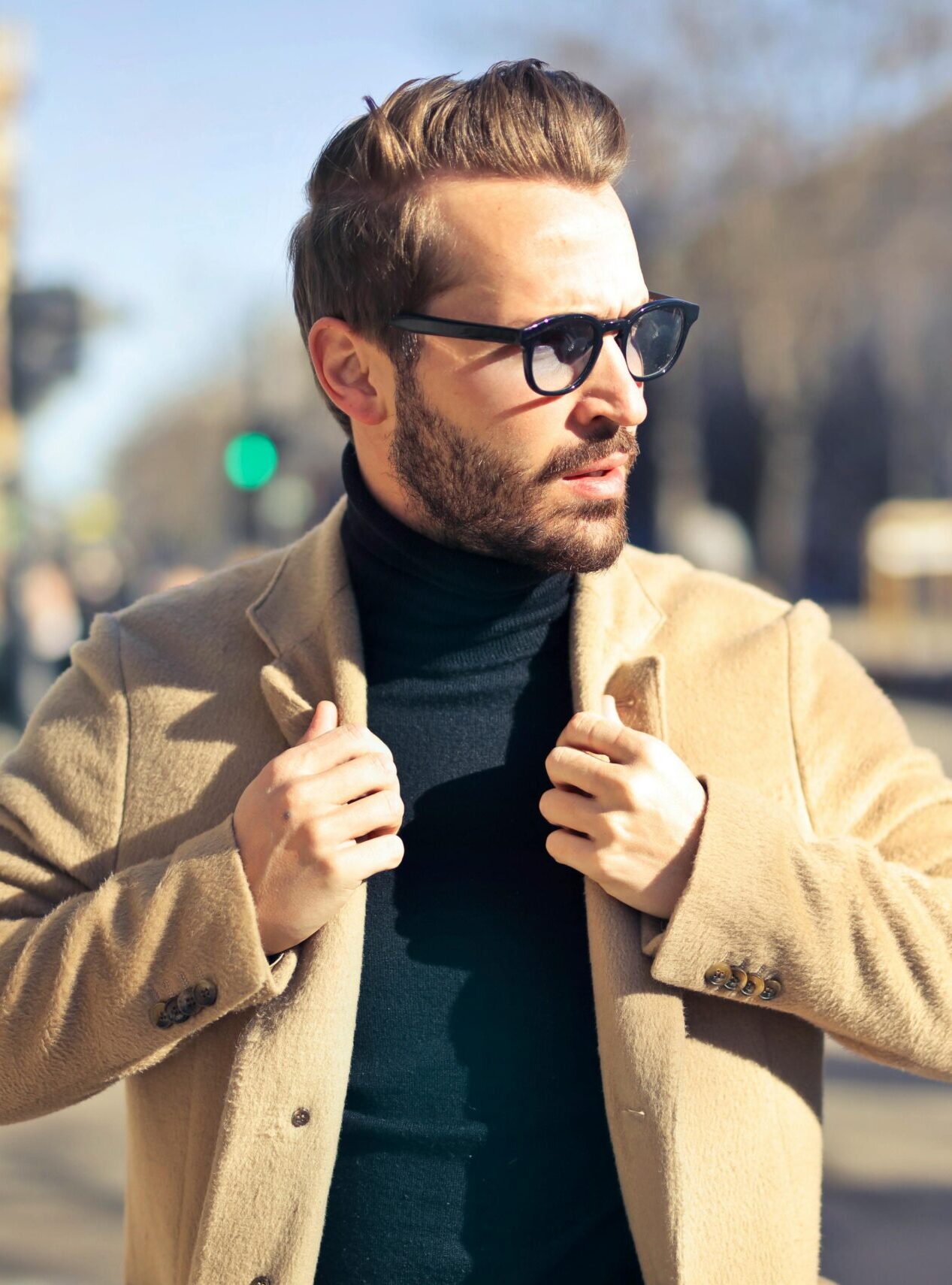 Fashionable young man with sunglasses poses outdoors in a sunny Budapest street scene.